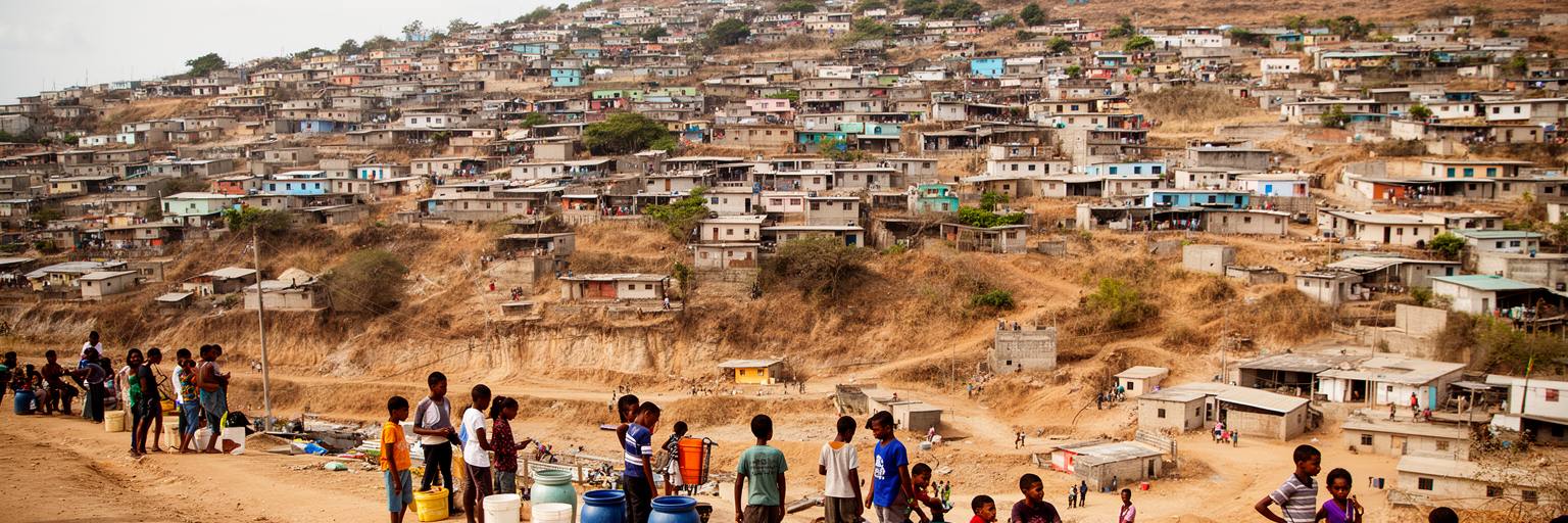 プライアの丘の住宅地、未舗装道路、若者、給水、公共施設が重なる生活景観